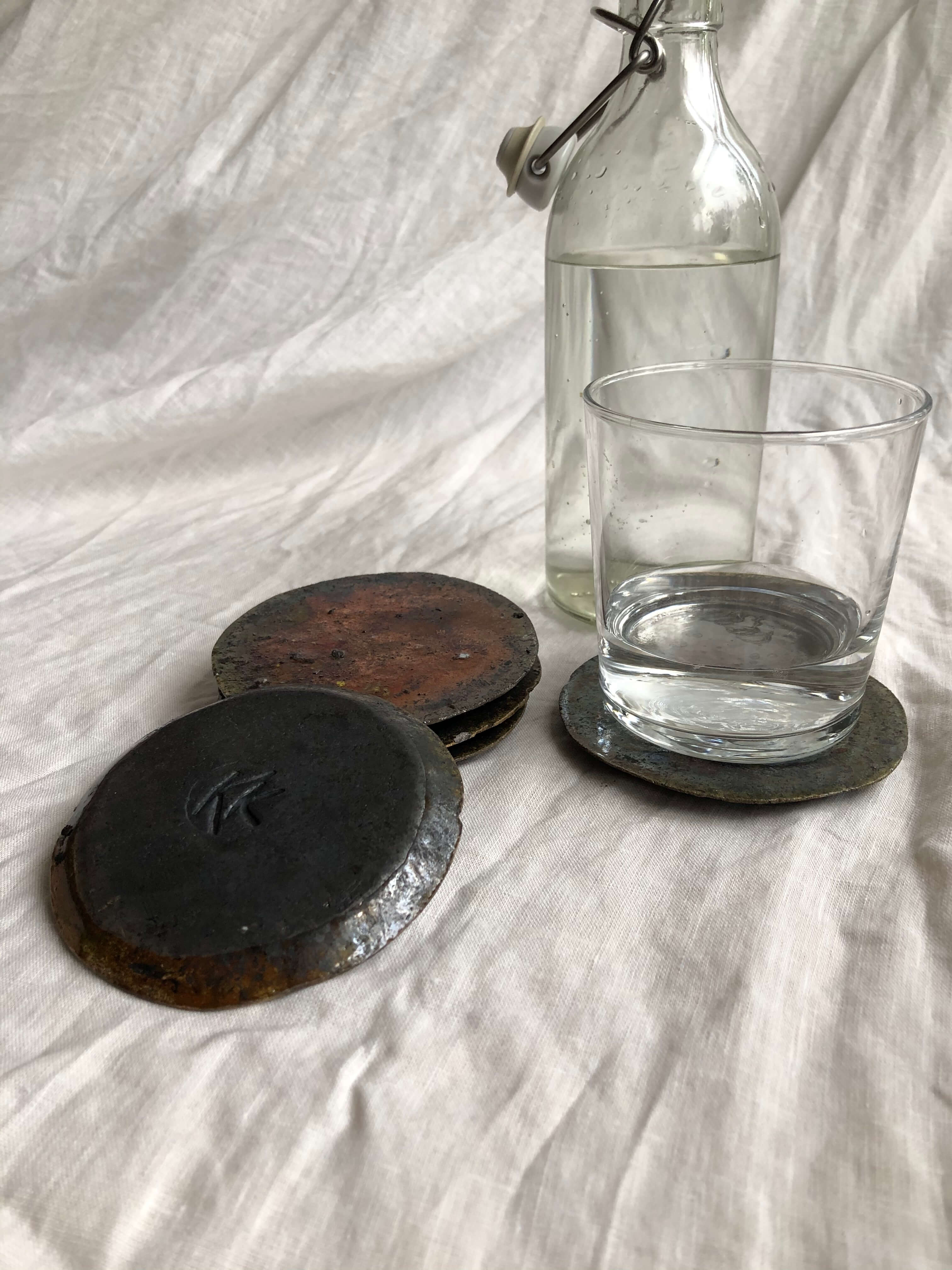 dark ceramic coasters, one with glass on it and glass water bottle next to it